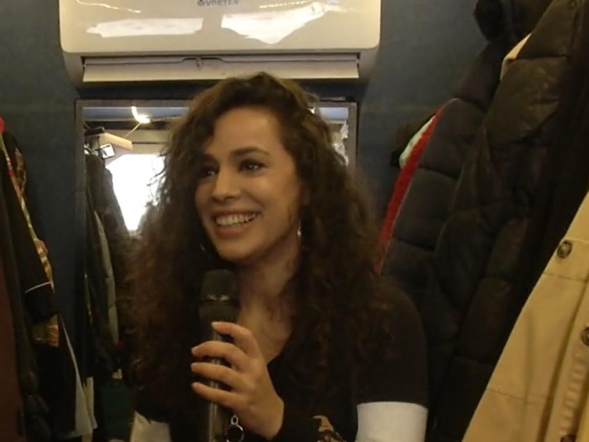 Alina Florescu ține microfonul în mână, zâmbește și se află într-o rulotă, pe platourile de filmare