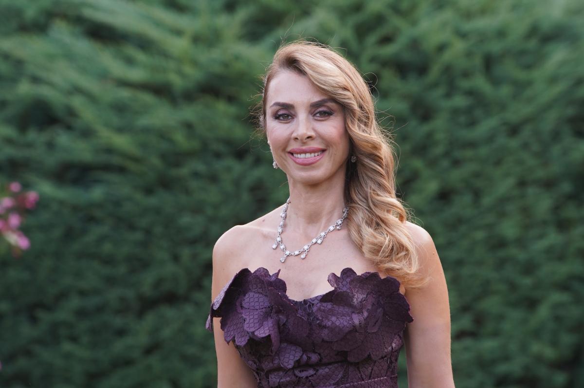 Neslihan Yeldan poartă o rochie mov, fără mâneci și are părul blond, desprins