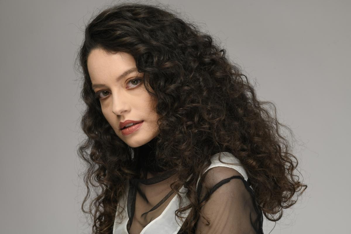 Gizem Arikan poartă o bluză transparentă și are părul lung, desprins și ondulat