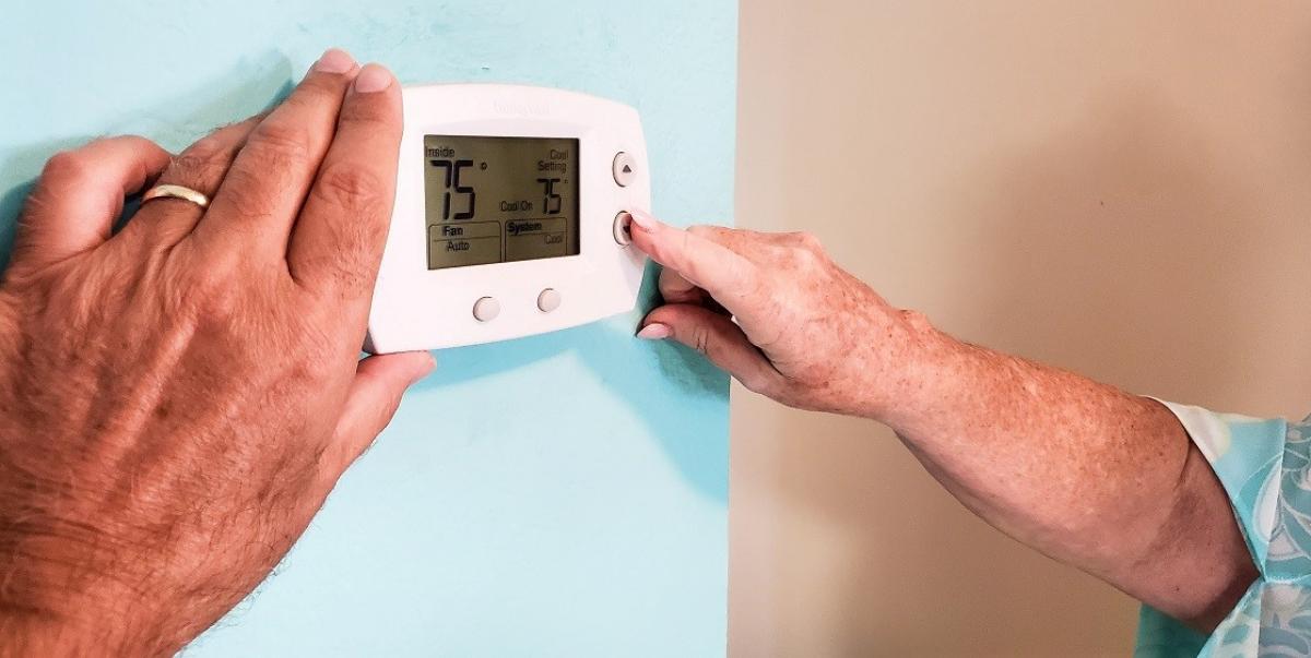 termostat pe perete apăsat de cineva cu degetul