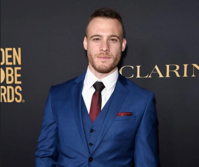 Kerem Bürsin poartă un costum albastru și cămașă vișinie