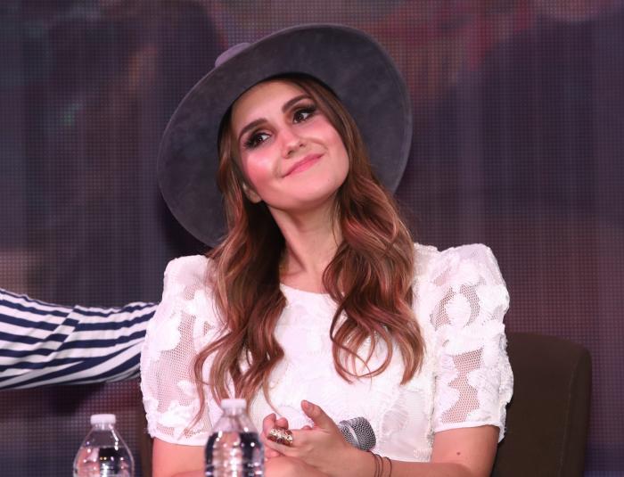 Dulce María poartă o rochie albă și o pălărie cu boruri largi