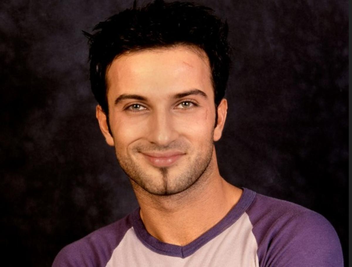 Tarkan zâmbește și poartă o bluză mov cu mâneci lungi