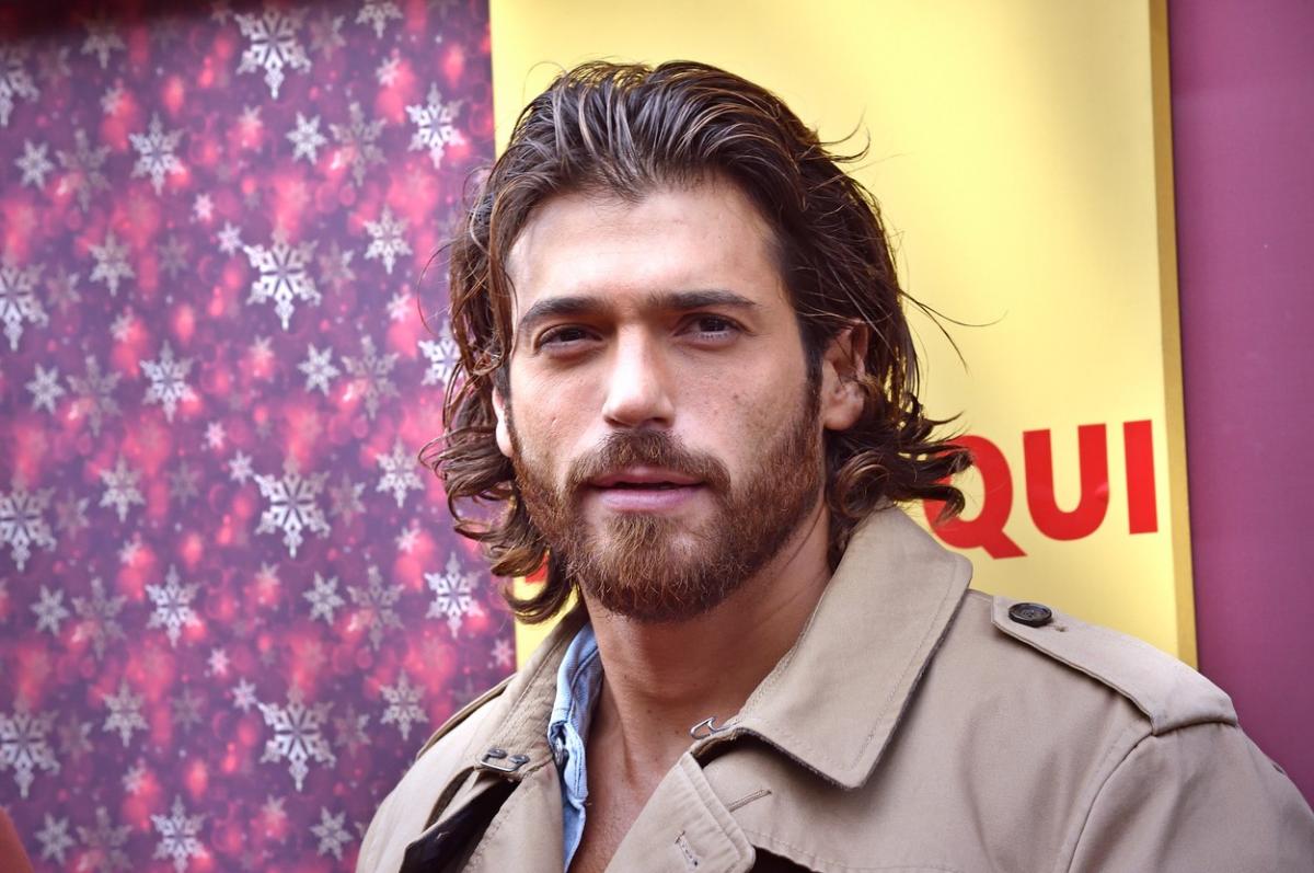 Can Yaman poartă un palton maro deschis și are părul dat pe spate, cu gel