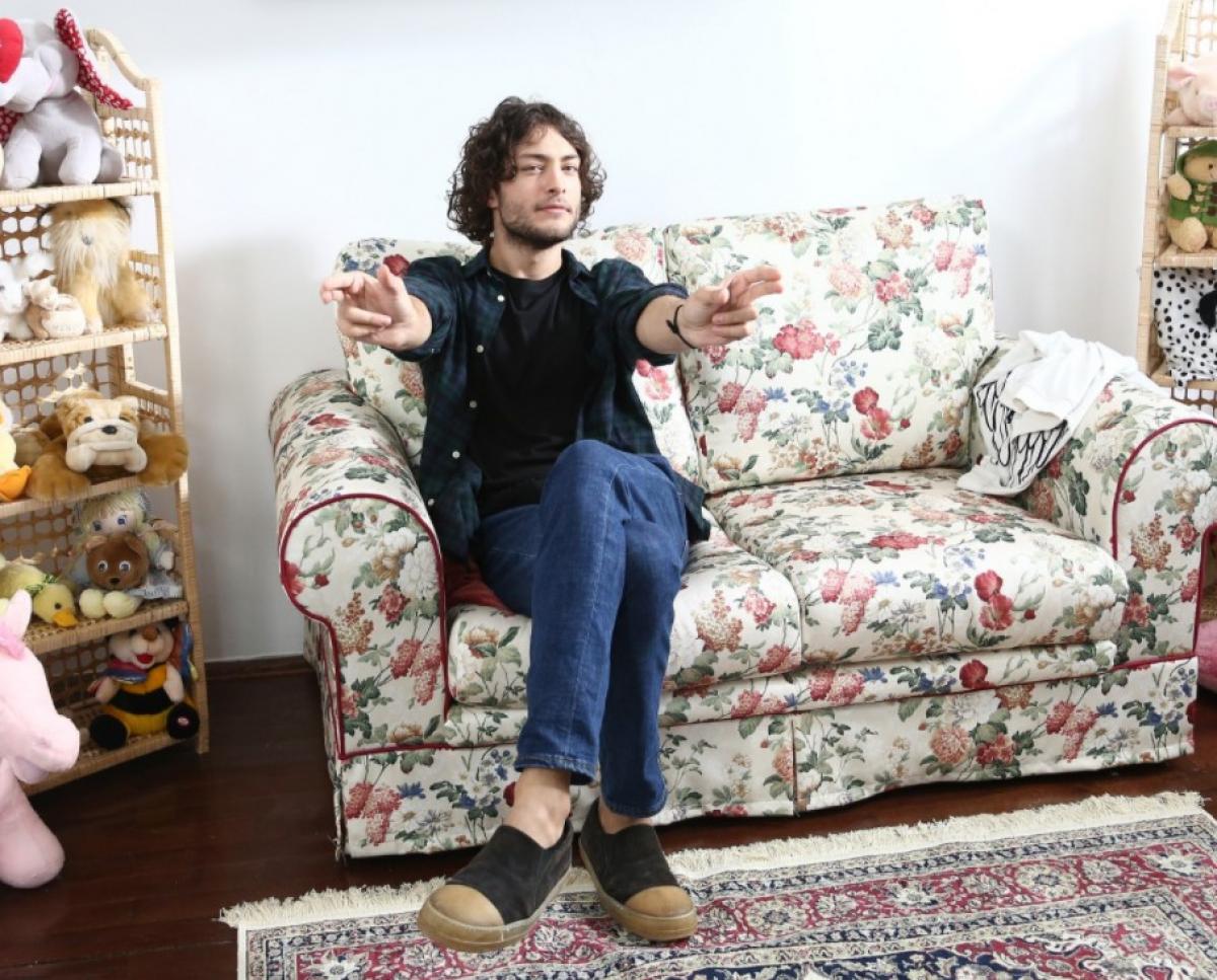 Toto Dumitrescu poartă blugi albaștri, sacou negru și întinde brațele către cameră