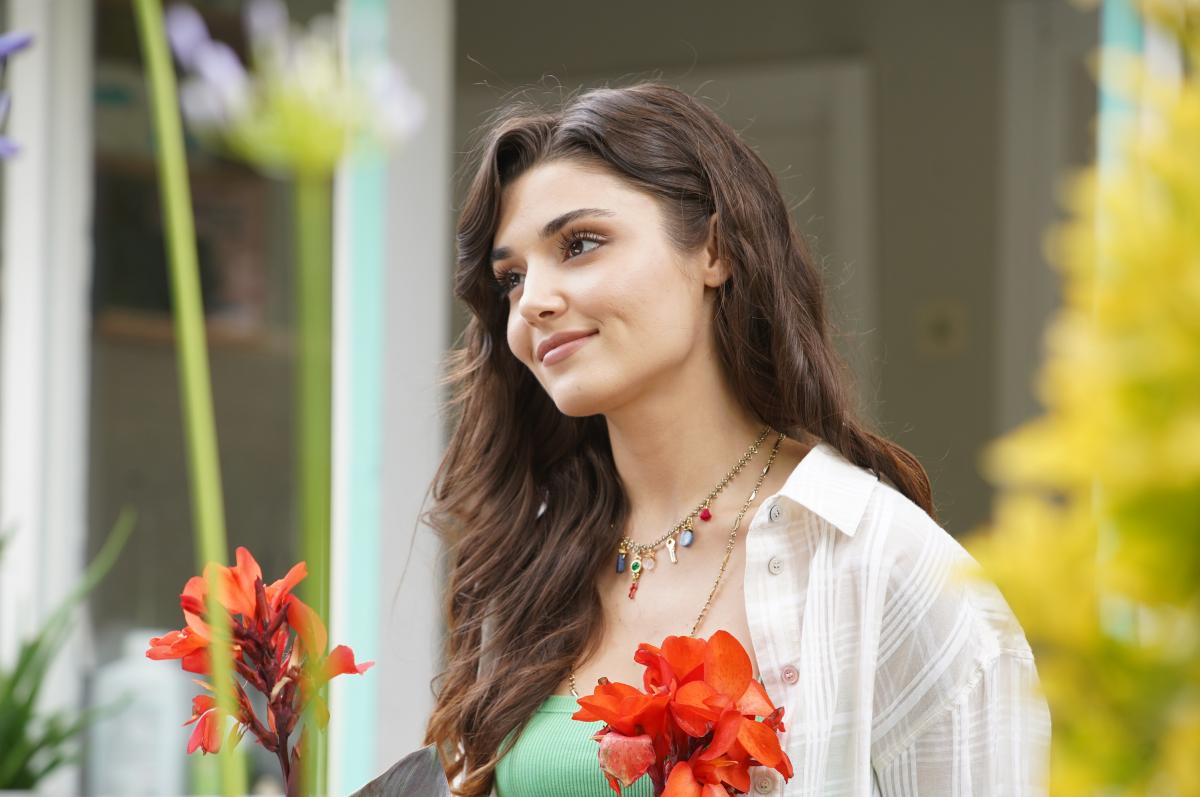 Hande Erçel poartă un tricou verde, o cămașă albă și are părul desprins.