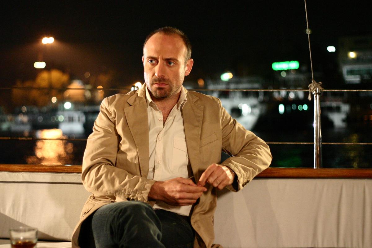 Halit Ergenç poartă o cămașă deschisă la culoare și un sacou maro deschis