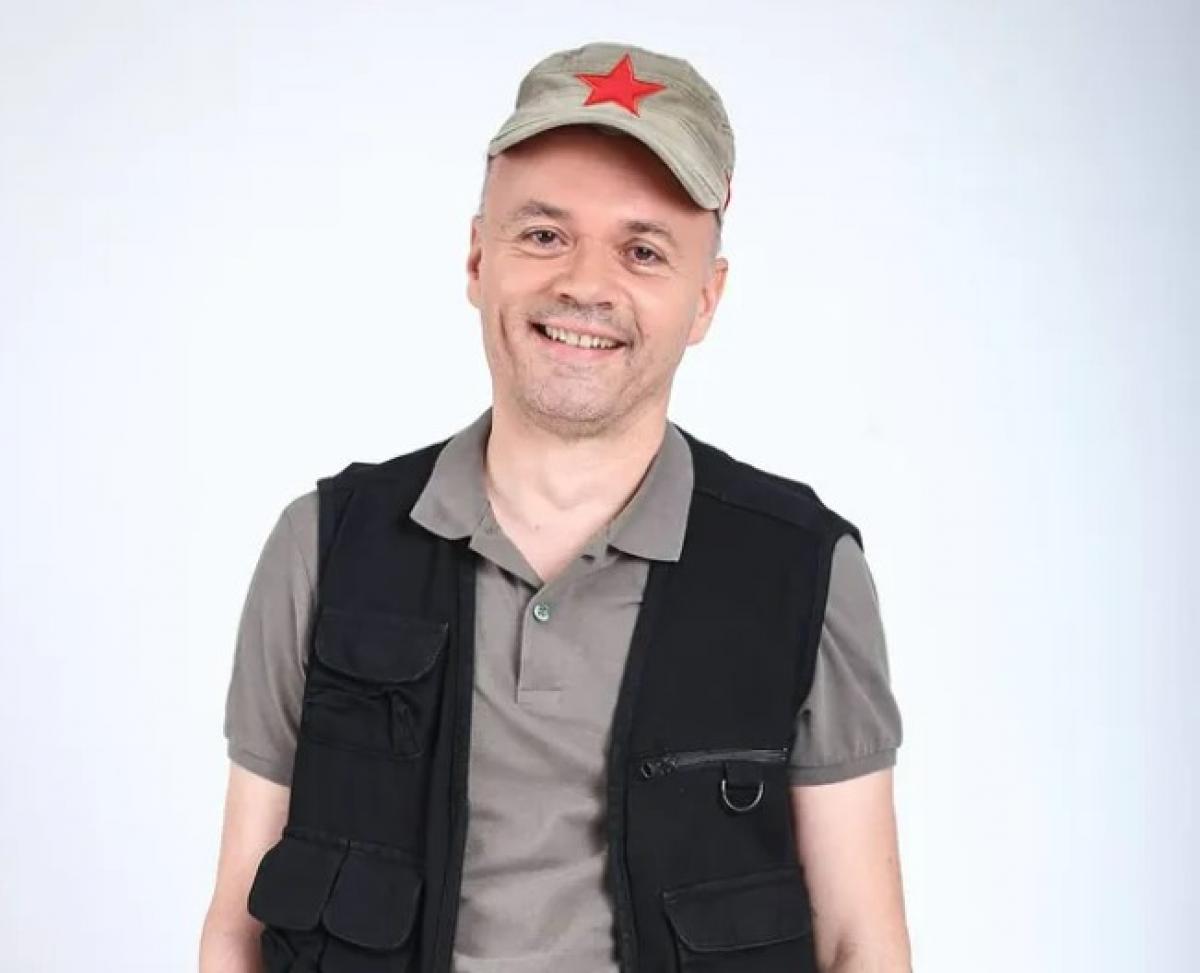 Mircea Gheorghiu poartă un tricou gri, vestă neagră și șapcă maro deschis