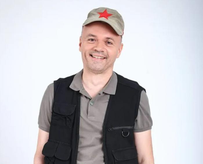 Mircea Gheorghiu poartă un tricou gri, vestă neagră și șapcă maro deschis