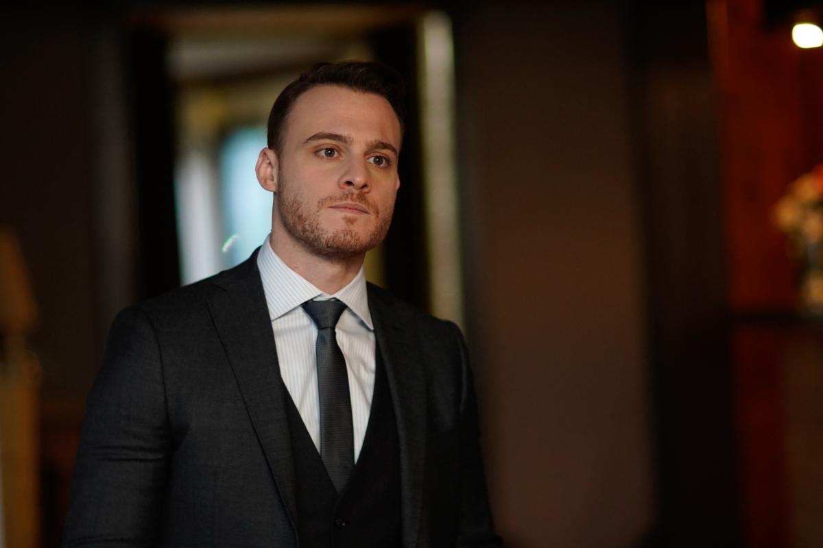 Kerem Bürsin poartă un costum negru, cămașă albă și cravată neagră