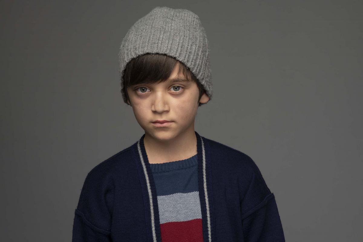 Erdem Eren Ayaz poartă un tricou colorat, hanorac închis la culoare și fes gri