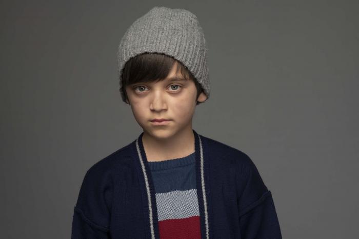 Erdem Eren Ayaz poartă un tricou colorat, hanorac închis la culoare și fes gri