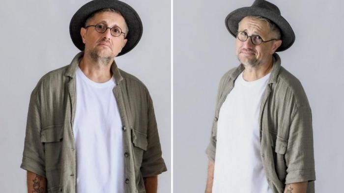 Bogdan Talașman poartă un tricou alb, o cămașă kaki, pălărie și ochelari de vedere