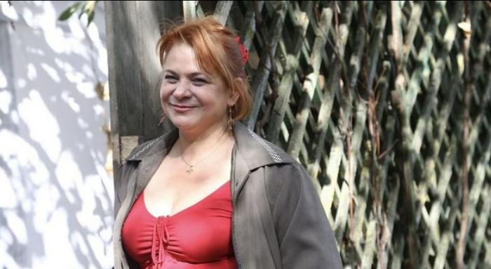 Anca Sigartău poartă o bluză roșie cu decolteu și un hanorac gri