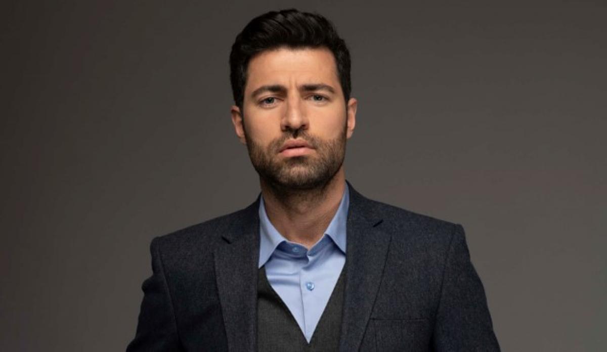 Emre Çaltılı poartă o cămașă albastră și sacou închis la culoare