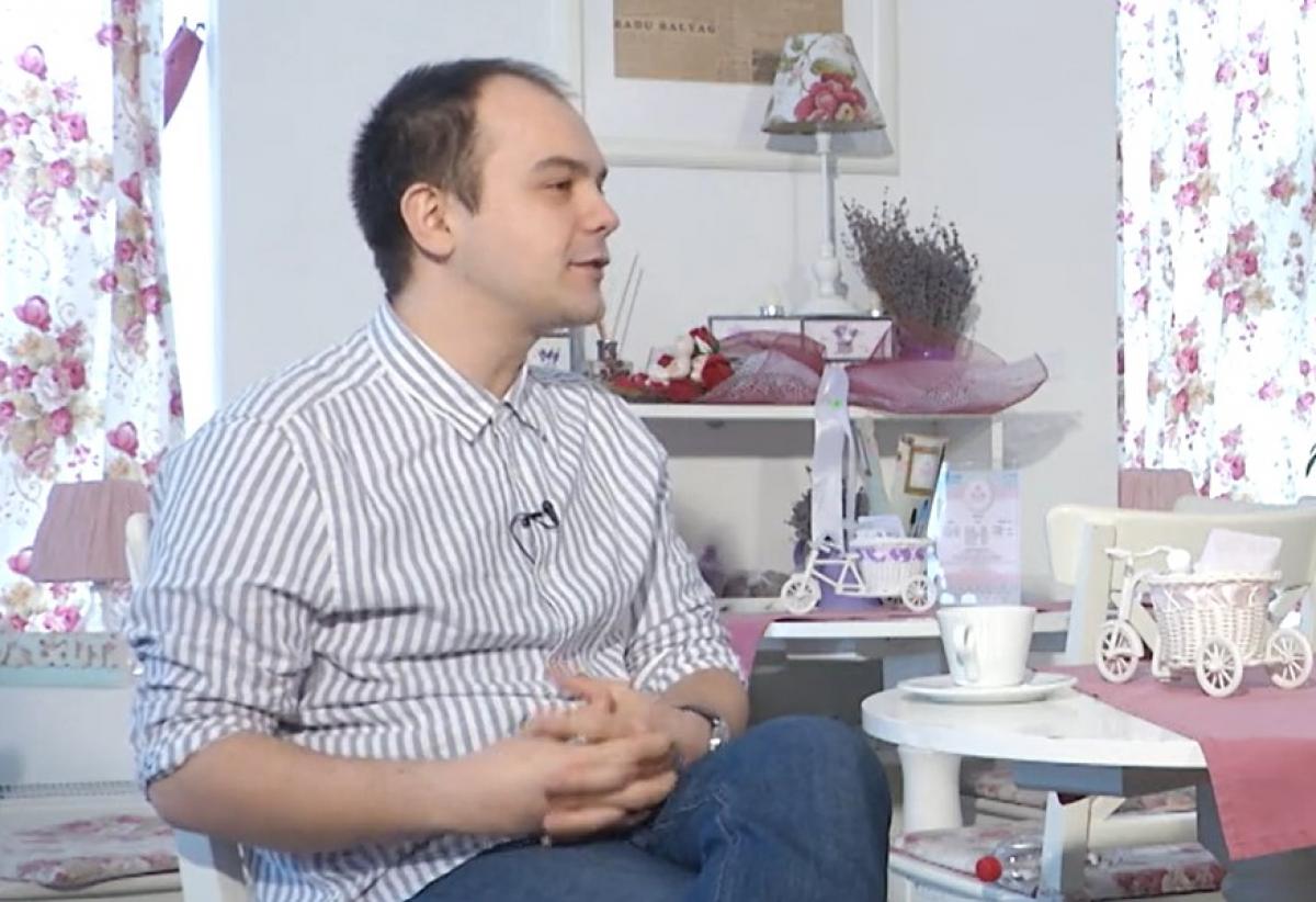 Andrei Huțuleac poartă blugi și cămașă și stă cu mâinile încrucișate