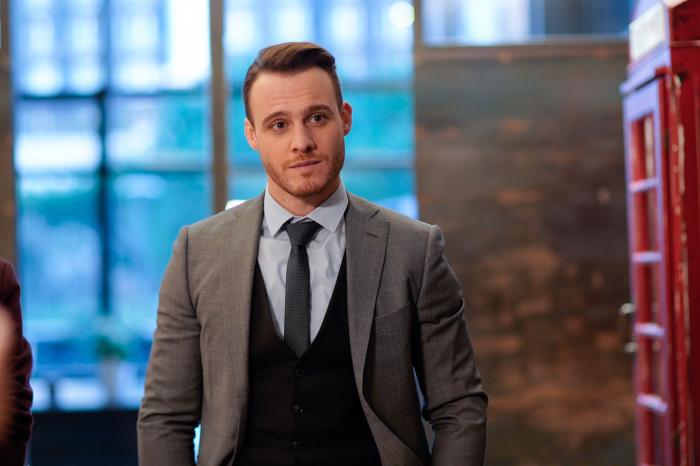 Kerem Bürsin poartă o cămașă albastră, sacou gri și o vestă neagră