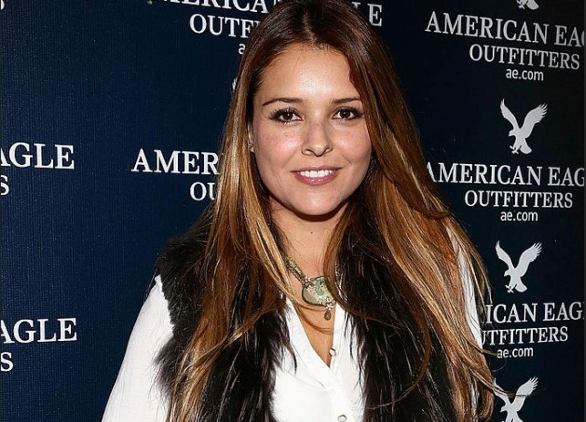 Grettell Valdez poartă o bluză albă și o vestă neagră de blană