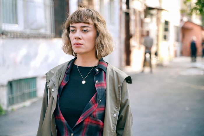Demet Evgar poartă un tricou negru, cămașă în carouri și o geacă