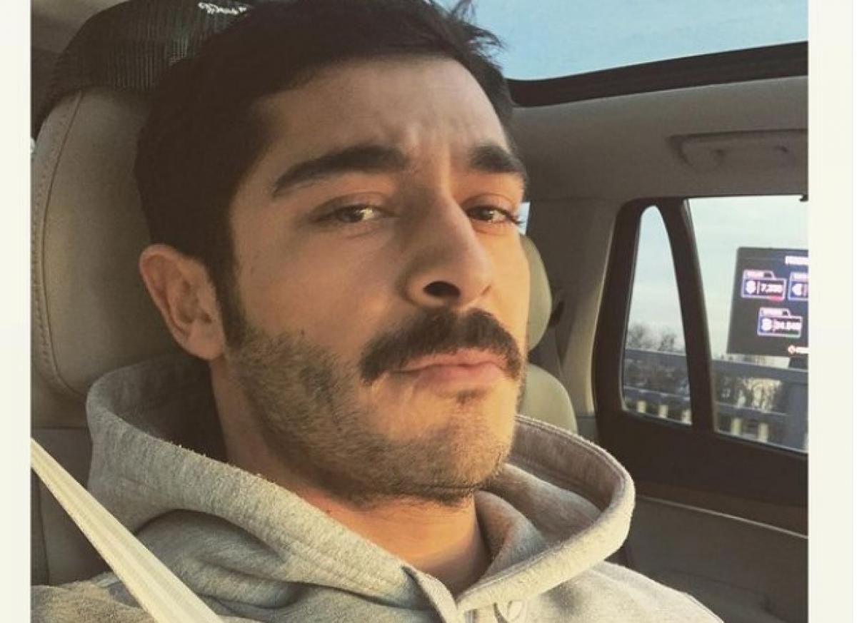 Burak Deniz poartă un hanorac, are mustață și se află într-o mașină pe locul din dreapta