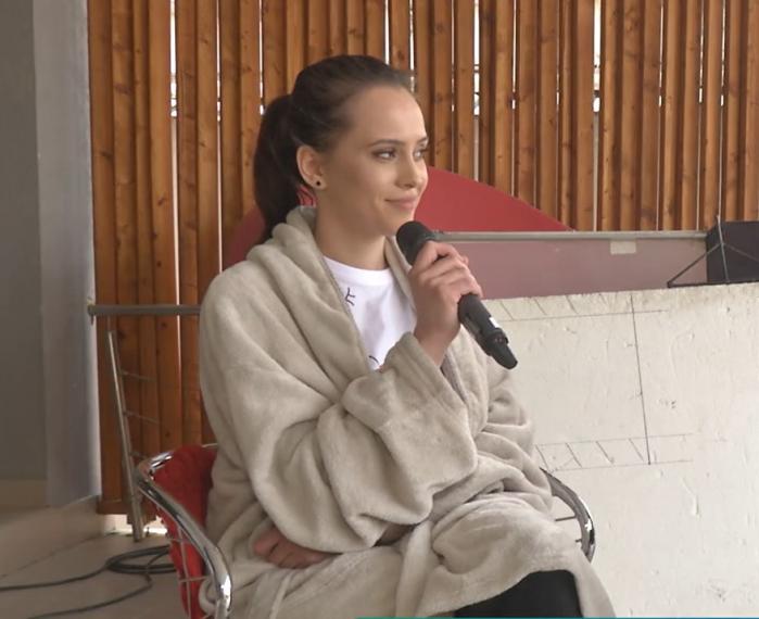 Claudia vasile poartă un tricou alb și un pulover maro. Are părul prins într-o coadă de cal
