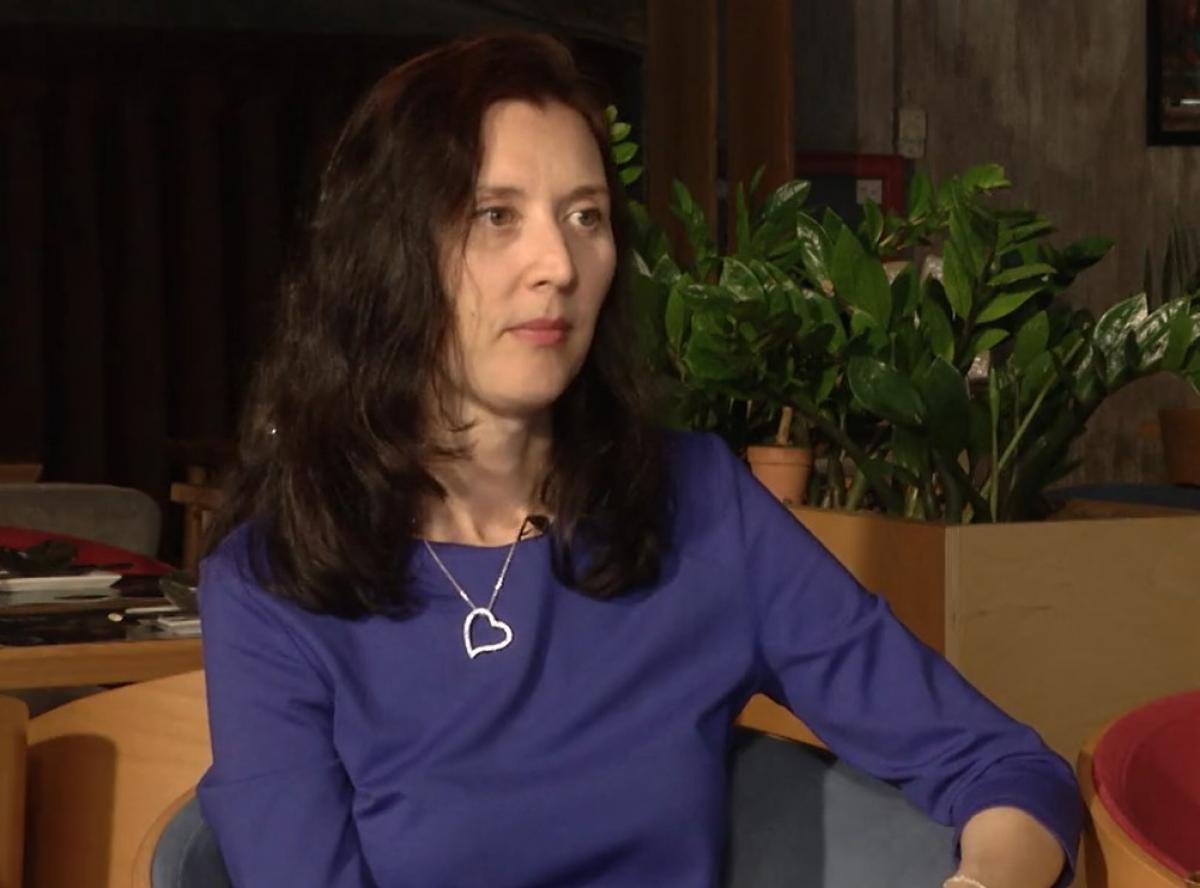 Raluca Mihăilă poartă o rochie albastră, lănțișor cu inimioară și părul lung, desprins