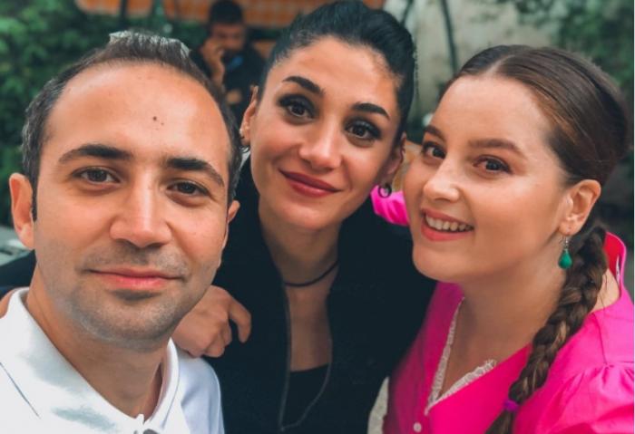 Sarp Bozkurt poartă o cămașă albă și se află alături de două dintre colegele sale din Dragostea plutește în aer