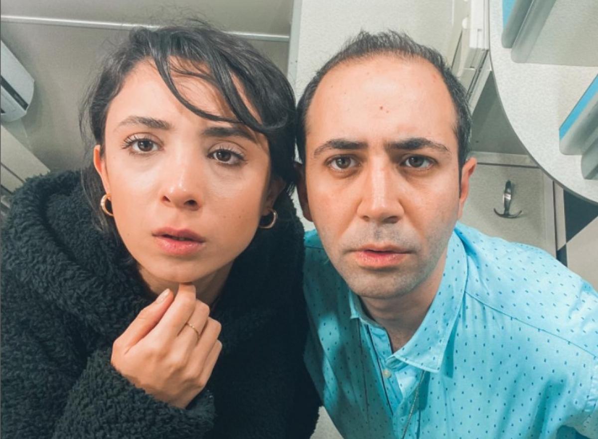 Sarp Bozkurt poartă o cămașă bleu și stă alături de una dintre colegele de platou din Dragostea plutește în aer