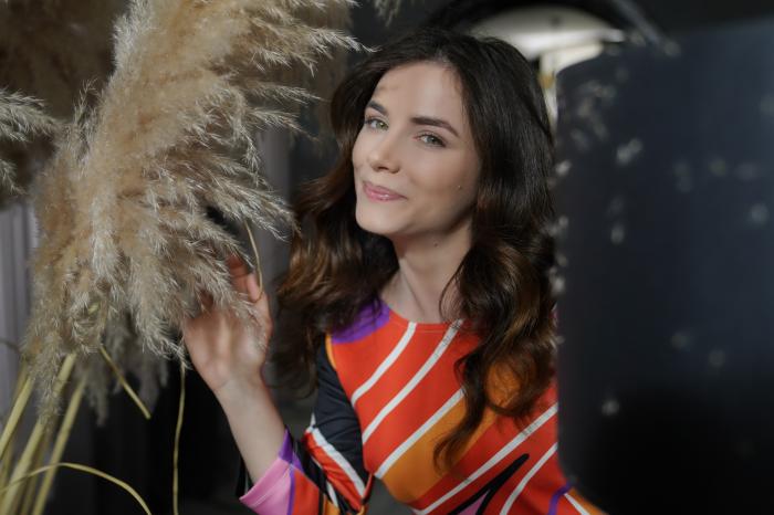 Cansu Tuman poartă o rochie portocalie cu dungi, are părul desprins și zâmbește