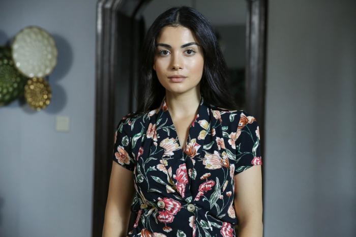 Özge Yağız poartă o rochie cu flori și are părul desprins și brunet