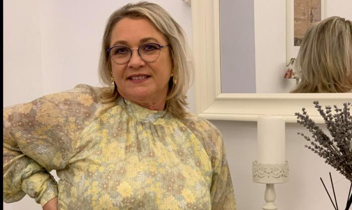 Georgeta Bucur este îmbrăcată cu o rochie cu flori și stă în spatele unei oglinzi