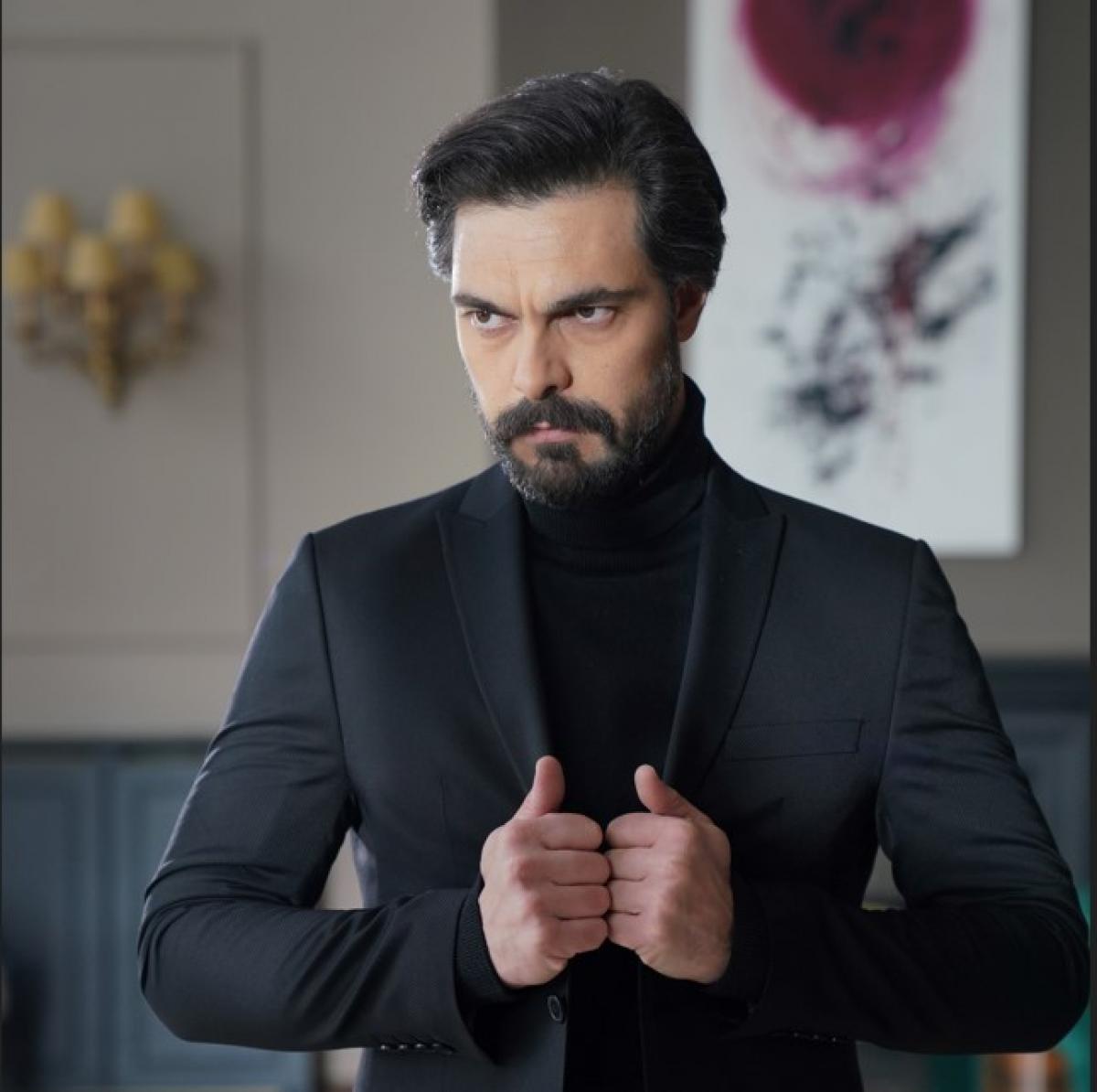 Halil Ibrahim Ceyhan poartă o maletă neagră și un sacou de aceeași culoare. Se ține cu mâinile de sacou și are o privire încruntată