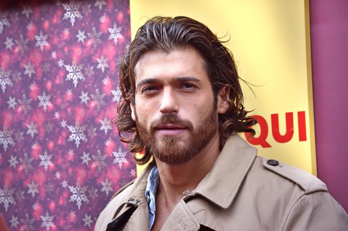 Can Yaman poartă un palton maro deschis și are părul dat pe spate, cu gel