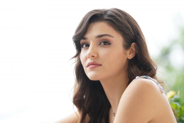 Hande Erçel poartă o rochie albă fără mâneci și se uită în depărtare. Actrița are părul desprins, ușor lăsate pe frunte în partea dreaptă