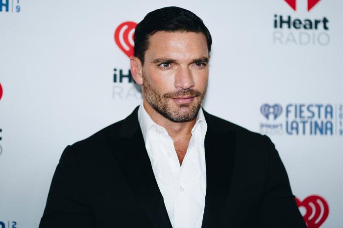 Julián Gil poartă o cămașă albă și un costum negru și zâmbește ușor