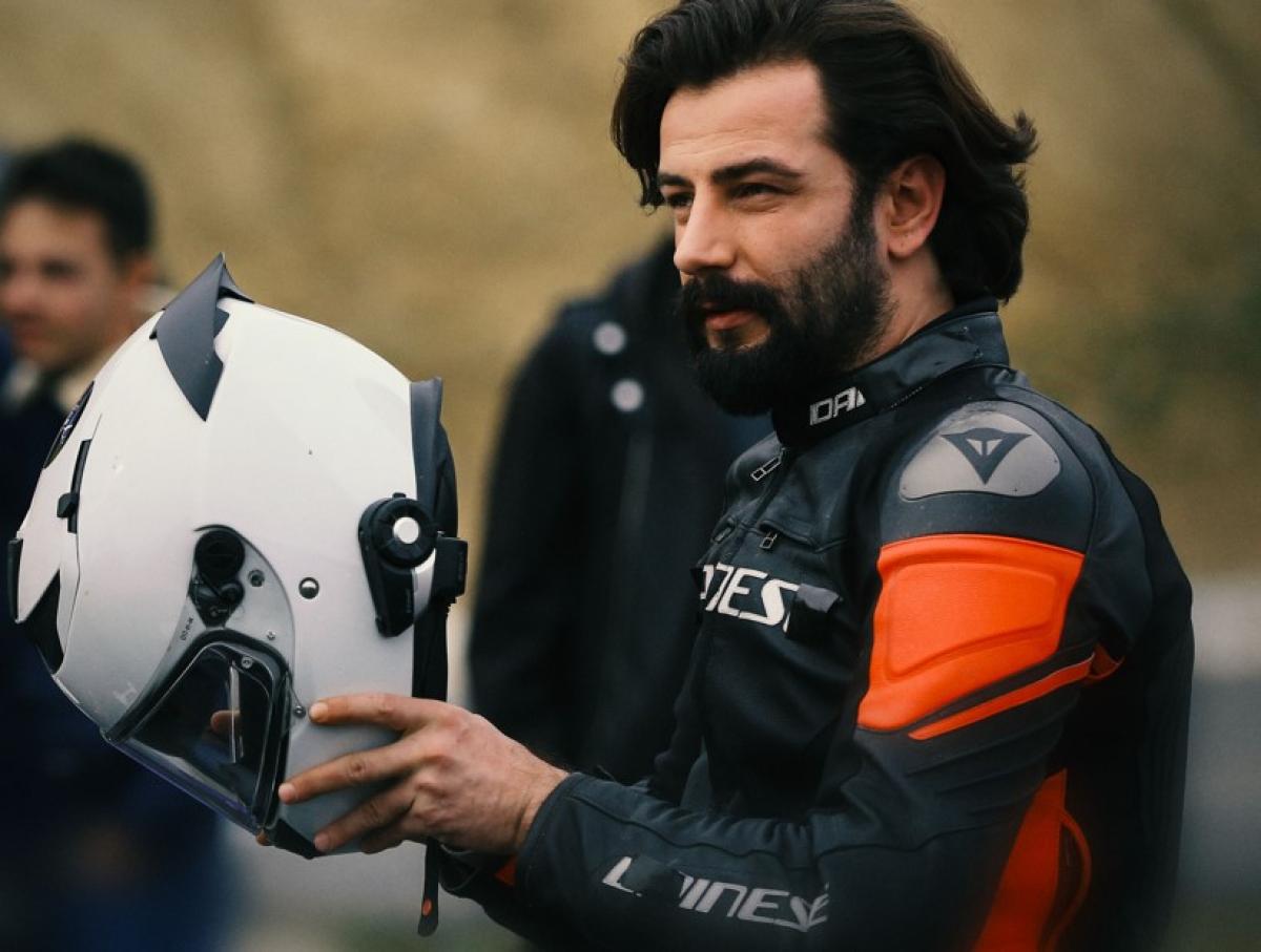 Gökberk Demirci poartă costum de motociclist și ține o cască în mână