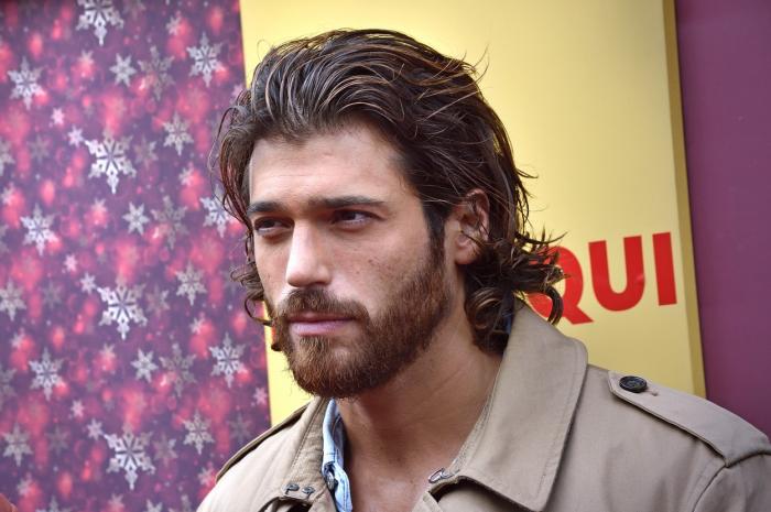 Can Yaman poartă un palton maro deschis și are părul dat pe spate, cu gel