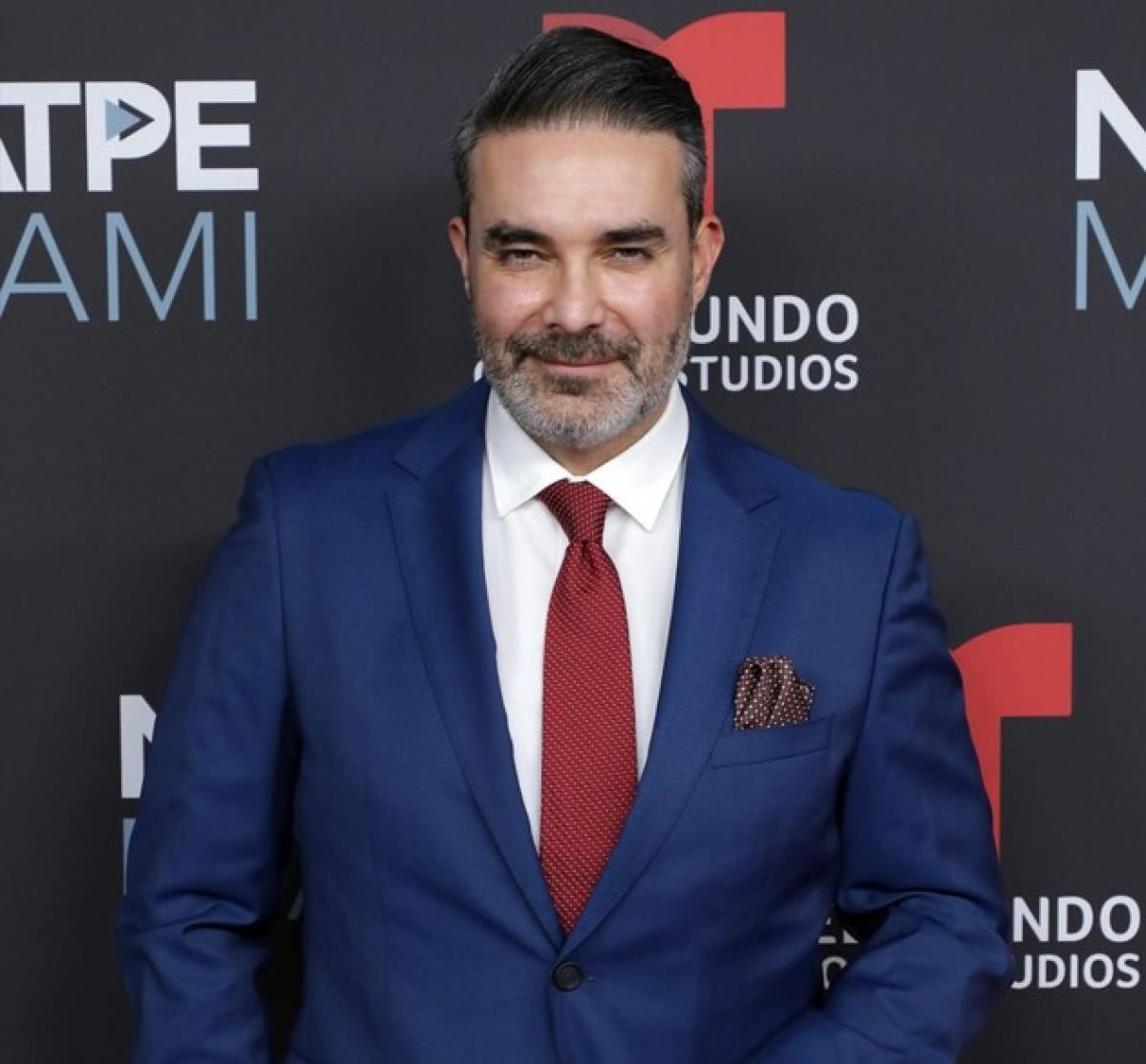 Mauricio Islas poartă o cămașă albă și un sacou albastru, dar și cravată roșie