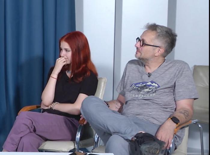 Bogdan Talașman poartă blugi și tricou gri și stă pe scaun lângă fiica sa, Maria