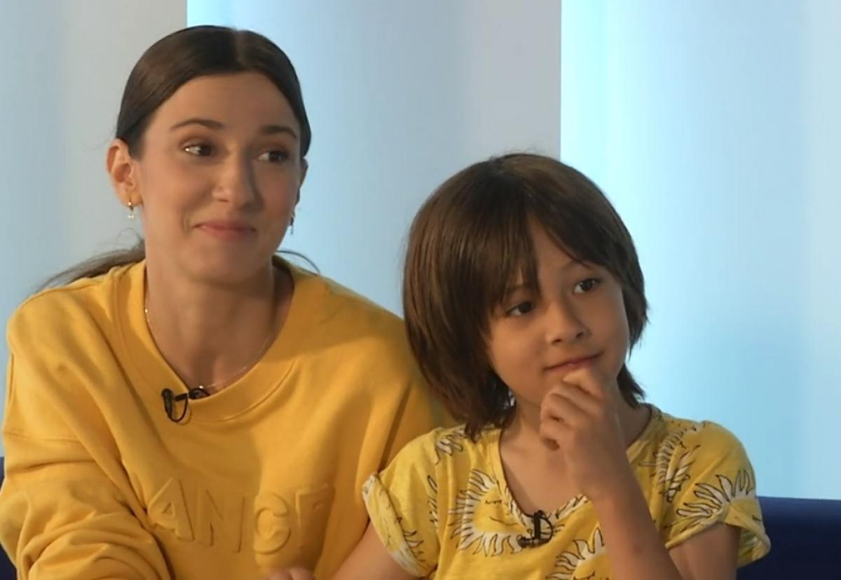 Dana Rogoz poartă un hanorac galben cu mâneci lungi și stă lângă fiul ei, Vlad care poartă un tricou galben cu imprimeu