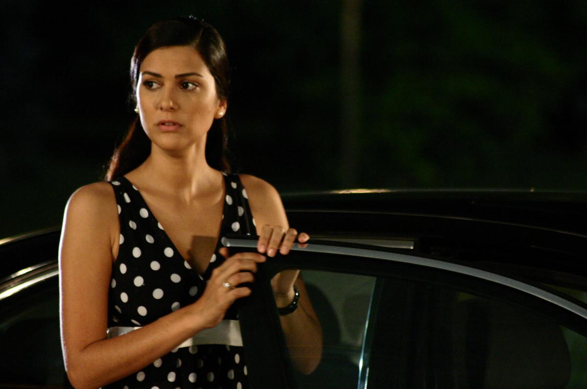 Bergüzar Korel poartă o rochie cu buline și stă cu mâna sprijinită de ușa unei mașini