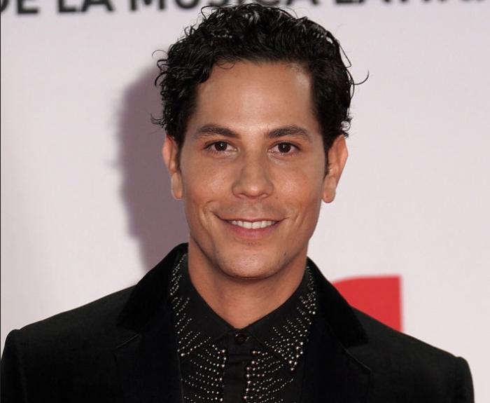 Christian Chávez poartă un costum negru și zâmbește