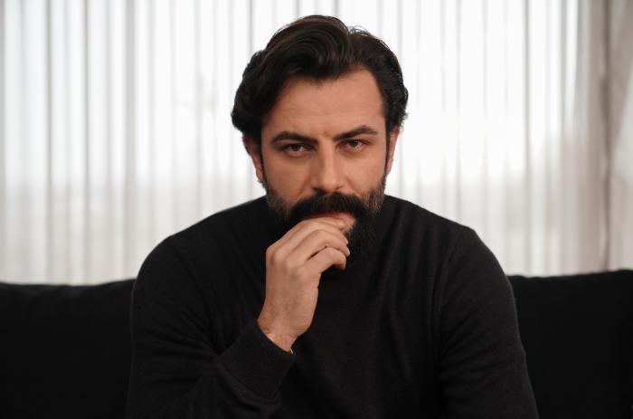 Gökberk Demirci este îmbrăcat în negru și își ține mâna dreaptă în dreptul gurii