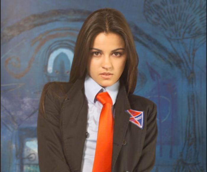 Maite Perroni poartă o cămașă albastră și un sacou negru, dar și cravată roșie