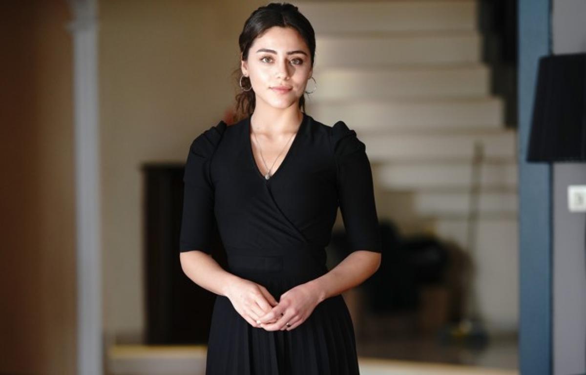 Sıla Türkoğlu poartă o rochie neagră și își ține mâinile împreunate și are părul prins într-o coadă de cal