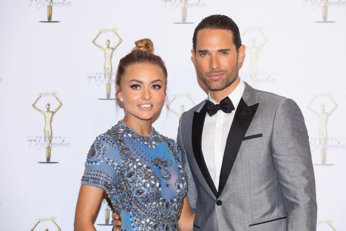 Angelique Boyer poartă o rochie de gală de culoare albastră și are părul prins într-un coc și stă lângă Sebastian Rulli care poartă un costum gri și are părul coafat cu gel