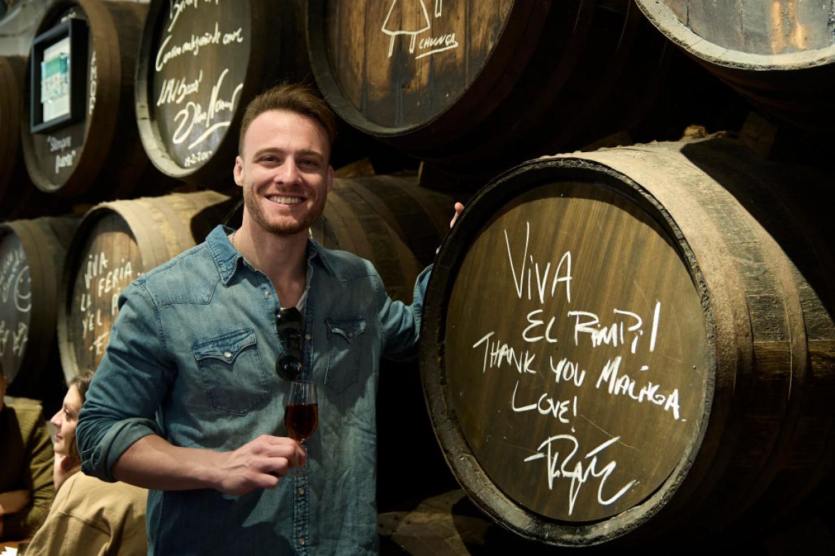 Kerem Bürsin stă în dreptul unui butoi pe care este transmis un mesaj și zâmbește