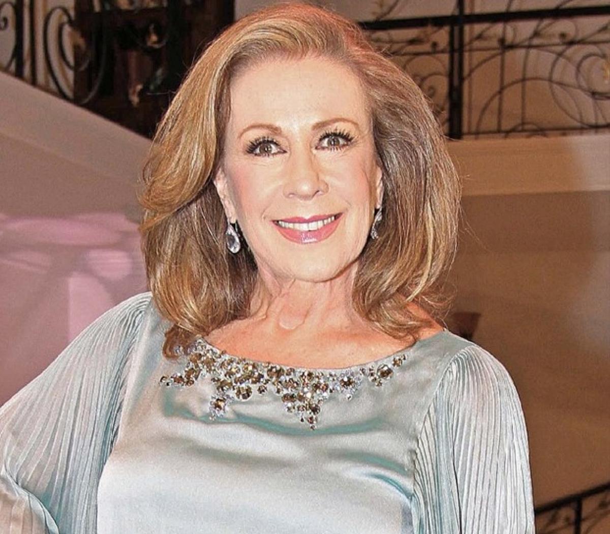 Laura Zapata poartă o bluză cu mânecă lungă și zâmbește