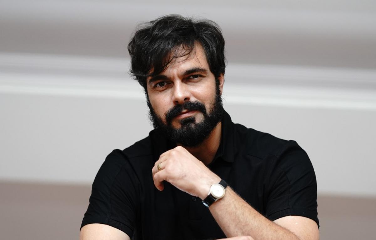 Halil İbrahim Ceyhan poartă un tricou negru și își ține mâna stângă în dreptul feței
