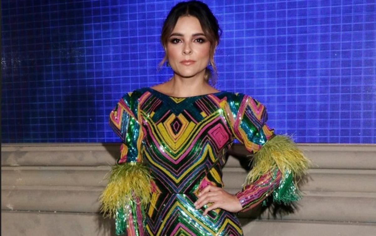 Grettel Valdez poartă o rochie colorată cu paiete și își ține mâna stângă în șold